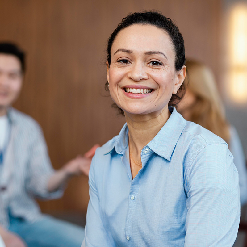 eine Frau sitzt vor einer Gruppe und schaut in die Kamera